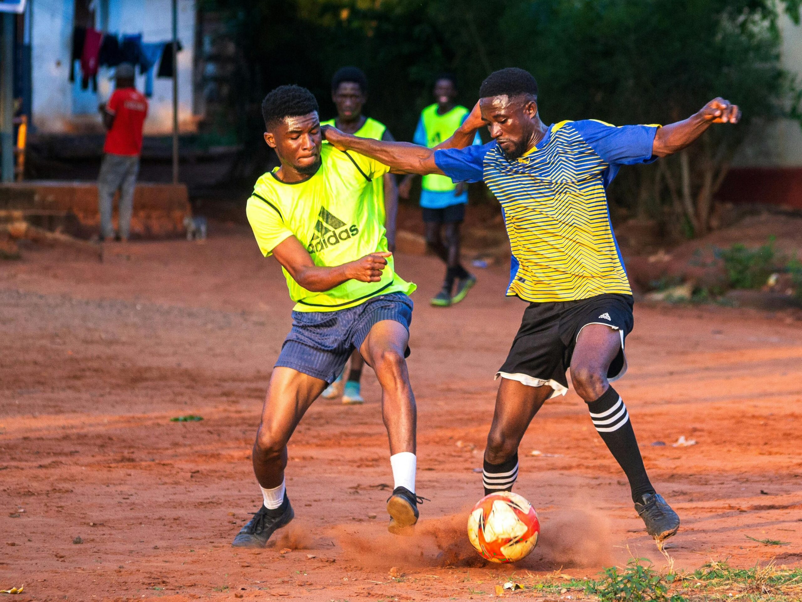 Player Representation Dynamic soccer game in Accra showing young athletes playing on a dirt field.
